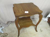 Full front view of antique oak table showing square tabletop with curved sides, curved legs, and lower shelf.