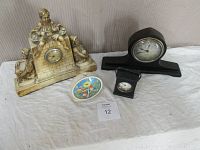 All four clocks shown together on table: plaster Boy on the Wall clock, Gilbert Tambour mantel clock, leather travel clock, and Smiths metal alarm clock.