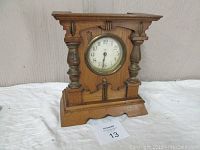 Front angle view of the maple wooden mantel clock with visible turned columns and round dial.