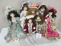 Seven dolls dressed in detailed period clothing posed on a white cloth. Dolls vary in size and costume colors.
