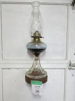 Full view of antique oil lamp with chimney on solid oak shelf showing overall structure and height.