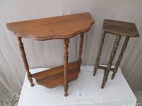 Two small occasional tables against a white backdrop: a taller pine plant stand with curved top and lower shelf, and a smaller, darker maple table with four turned legs.