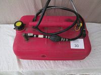 Red Wedco outboard motor gas tank with attached black Johnson gas line, primer bulb, and connector, shown on white surface.
