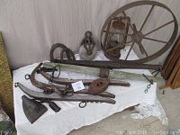 Photo showing the steel wheel, lantern, pulley, irons, yokes, and other metal yard art items on white cloth.