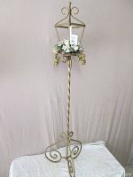Full view of tall wrought iron candle stand with satin gold finish, showing scroll work base and hexagonal lantern top with floral decoration.