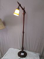 Full view of wooden floor lamp standing lit showing cherry finish and round base