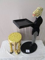 Photo of lazy butler figure stand holding the black rectangular serving tray standing next to the plaster giraffe stool showing their relative size and details.