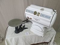 Side view of white Fairbanks Morris Chicago scale on a white cloth surface showing circular weighing platform and metal base.