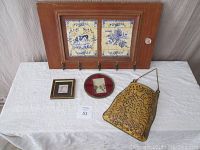 Wooden hat rack with porcelain tile inlay, two small framed prints, and metal flower holder on white cloth background.