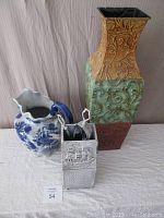 Photo showing three items: tall decorative stamped vase, cobalt blue jug with floral design, and white antiqued brass fireplace tool set.