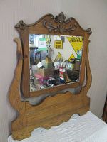 Victorian oak framed bathroom mirror with carved wooden scrollwork and beveled glass showing reflection of background items.