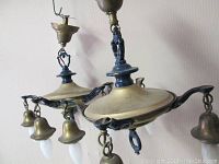 Two antique Victorian style hanging light fixtures composed of brass and cast metal, showing ornate detailing and brass bell-shaped accents housing bulbs with frosted covers