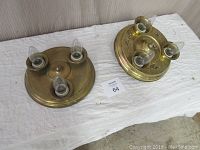 Two Victorian style solid brass 3-light fixtures on white cloth showing overall condition and arrangement