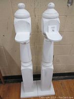Front view of two antique newel posts painted white, showing overall height and base shape.
