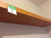 Close-up photo of one maple-colored wooden shelf with an orange-green sticker showing number 8. Shelf has a smooth finished surface and appears lightly used.