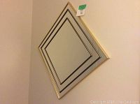 Front view of diamond shaped mirror with gold and black trim hanging on wall.