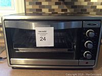 Front view of Oster stainless steel toaster oven showing control knobs and glass door.