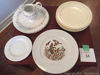 Top view of plates stacked including gold rim plates, white plates with blue floral and silver accents, wild geese plates, and small plain white plate with matching creamer on top