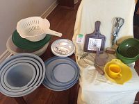 Overview of all kitchen items including bowls, plates, colander, cheese board, potato masher, measuring cup, egg beater, yellow bowl and cup