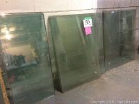 Three large thick glass sheets leaning against a wall, showing their thickness and size.