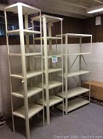 Front view of three white metal shelving units placed side by side in a basement room with concrete walls and wood paneling.
