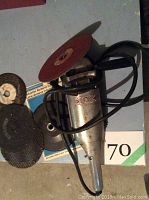 Photo showing ROX electric grinder/sander with red abrasive disk installed, accompanied by multiple used grinding and sanding disks.