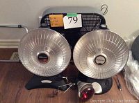 Photo showing large black box fan, two parabolic heaters, and brooder lamp with red bulb and mounting clip.