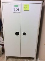 Closed IKEA white wardrobe storage unit with two doors and circular cut-out handles, left door flange missing.
