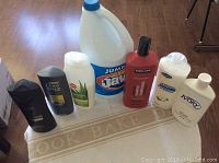 Seven bottles arranged on a table including a gallon jug of Jax bleach, Dove Men+Care body wash, Axe Excite body wash, Kirkland shampoo conditioner, Ivory lotion, and other shampoo and body wash bottles.