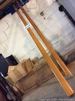 Two long solid wood handrails displayed against a wall, varnished and rectangular with moderate width.