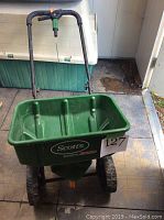 Full view of Scotts Speedy Green 3000 lawn seeder showing green seed hopper, handle and wheels.