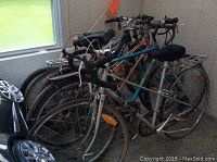 Three adult bicycles showing wear, rusted chains, and flat tires indoors near window.