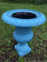 Full view of blue painted cast iron planter on grass with black liner pot inside.