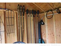 Photo showing three bamboo tiki torches and five metal tiki torches mounted inside shed, plus metal garden trellis leaning on wall.