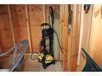 Full view of yellow and black Karcher pressure washer model 330 in wooden shed corner with hose and cords wrapped.