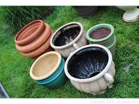 Overview of all seven planters including glazed stoneware, terracotta, and plastic pots placed on grass.