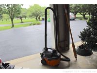 Side view of the Ridgid portable vacuum showing orange and black body with attached hose and handle.