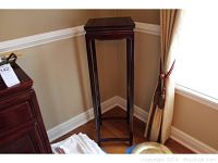 Full view of the wooden Asian plant stand positioned in a corner against beige walls with white trim, showing its height and slender legs.
