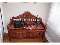 Front view of carved wooden bench with two drawers and decorative fabric seat showing overall design and scale, with several decorative objects displayed on seat.