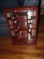 Frontal view of the wooden wall display cabinet showing the glass door and interior tiered shelves.