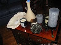 Overview of assorted candles, pottery barn blue grey candles in iron holders, cream-colored vase, and ceramic platter on wooden surface