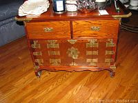 Front view of the Asian style wooden cabinet showing two drawers on top with brass handles and two lower doors with decorative brass hinges and lock.