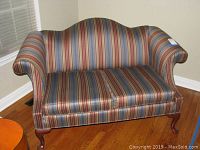 Front view of the striped upholstered loveseat showcasing its curved backrest and rolled arms.