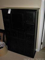 Front view of black wooden cabinet showing 14 drawers and central door