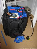 Black and blue diving bag with regulator hoses and compass on top, placed indoors on carpet