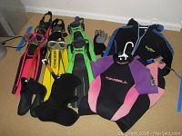 Photo of wetsuits, fins, snorkels, masks, gloves, shoes, and hood arranged on carpeted floor