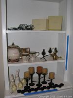 Shelving unit with multiple home decor items including string lights boxes, ceramic cookie jar, mugs, candle holders and candles, and small figurines