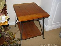 Side angle of a wooden top end table with metal legs showing wooden bottom shelf.
