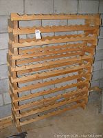 Full view of the wooden wine rack system standing on a concrete floor, showing multiple stacked shelves with scalloped bottle rests.