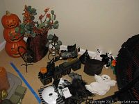 Wide view of Halloween decorations including pumpkin stack, 'BOO' sign, candle holders, spider, white ghosts, witch hat, and masks on a shelf in a room corner.
